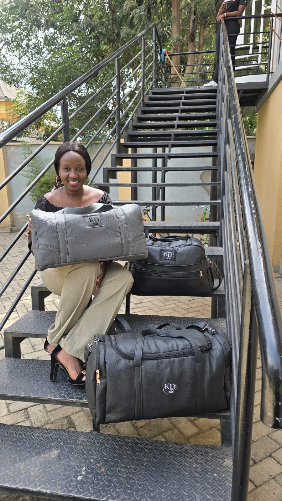 A woman seated on a staircase with grey and black Kai duffel bags